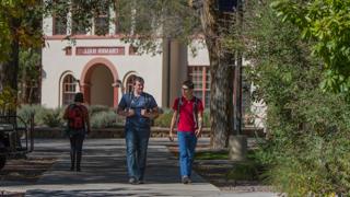 Image of two male students walking on the sidewalk. A tan adobe classroom building can be seen behind them. This is a link to the NMT Alternative Licensure Program